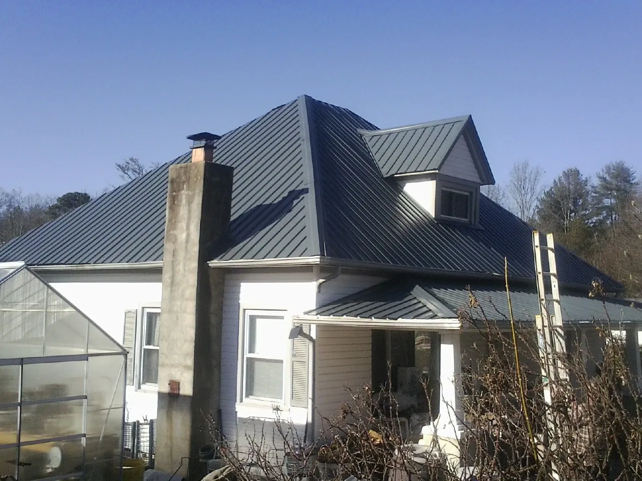 Dark blue standing seam metal roof on a white farmhouse with dormer — Slate & Tile Roof Repair by Roofing Brothers in Atkinson