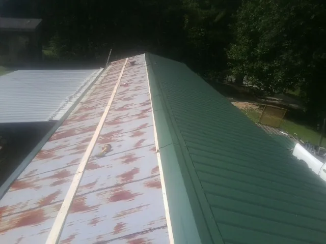 Old rusted panels beside newly installed green metal roofing — Wind Damage Roof Repair by Roofing Brothers in Atkinson